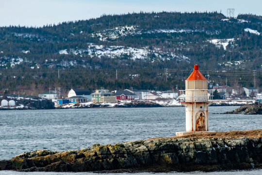 A Vintage Caisson Style Tower With A Round Red Metal Roof.  In The Center Of The Lighthouse Is A Vintage Lamp Made Of Multiple Pieces Of Glass. A Catwalk Made Of Metal Is Around The Beacon.