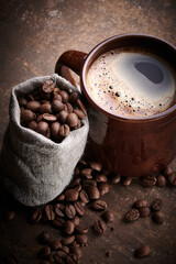 Composition of freshly brewed cup of coffee and roasted coffee beans in bag on brown background