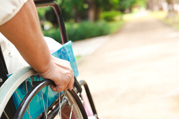 An elderly person sits in a wheelchair during a walk in the park on a sunny day. Persons with disabilities are accessible anywhere in public places where wheelchair access is available.