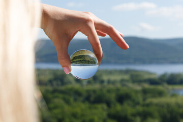 A look at the upside-down world through a ball. The girl's hand holds a crystal ball in which the image of mountains is inverted. Focus on the crystal ball. Take care of nature. Close-up