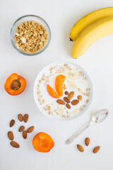 Granola breakfast with milk, fruits and almonds in the white bowl on the white tablecloth. Top view. Closeup. Location vertical.