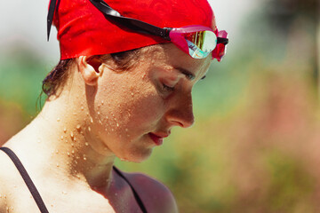 Closeup sportive woman, swimmer in cap and googles getting ready to start of swim at open public...
