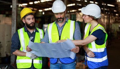 Male and female engineers chat with factory workers as they use machine drawings, planning for industrial maintenance