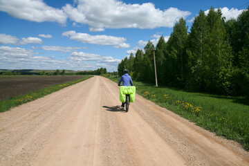 A cyclist rides on a dirt road among fields and forests, Bashkiria, Russia. 