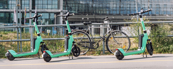 Many modern green electric scooters sharing parked city street. Self-service street transport...