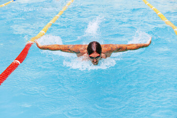 Young muscular man, professional swimmer in goggles training at public swimming-pool, outdoors. Sport, power, energy, style, hobby concept.