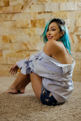 Sensual blue hair young model sitting on the floor of a studio and wearing and oversized shirt looking fun confident and comfortable while posing 