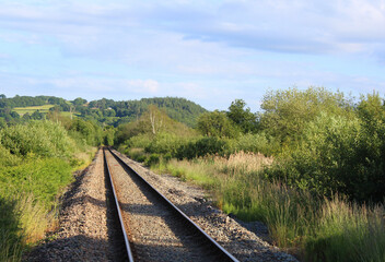 Fototapeta na wymiar railway tracks in the Welsh countryside, Image shows a long straight railway track going out of view with bushes either side and the Welsh hills in the distance