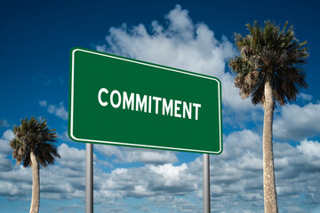 Fototapeta premium Highway sign with the word Commitment on a beautiful blue sky background with palm trees. Motivational concept for finding what we want on the journey of life.