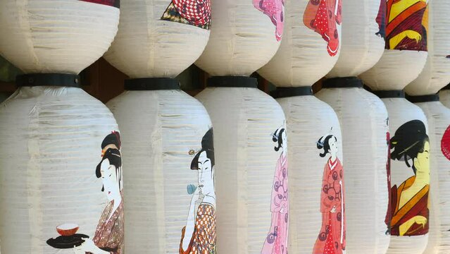 Traditional Japanese paper lanterns hang in the garden with mountains on background. Chochin lantern from Japan with pictures of women