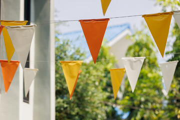 white, yellow and orange triangle flags hang on white rope in garden view. garland flag.concept : fun party.