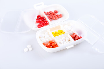 Pill box with colorful pills and vitamins. Plastic white container with cells for medicines. Health concept. Selective focus, close-up.