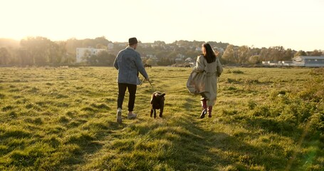 Rear view of a couple with a dog walking on pasture - Powered by Adobe