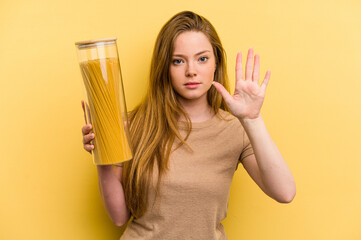 Young caucasian woman holding a spaghettis jar isolated on yellow background smiling cheerful showing number five with fingers.