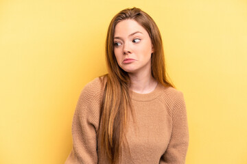 Young caucasian woman isolated on yellow background shrugs shoulders and open eyes confused.