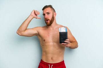 Young caucasian man holding a passport isolated on blue background feels proud and self confident, example to follow.