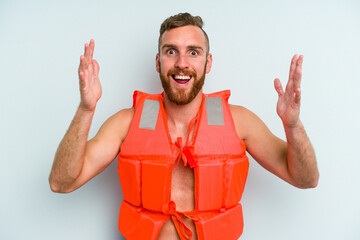 Young caucasian man wearing life jacket isolated on blue background receiving a pleasant surprise,...