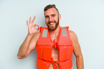Young caucasian man wearing life jacket isolated on blue background cheerful and confident showing...