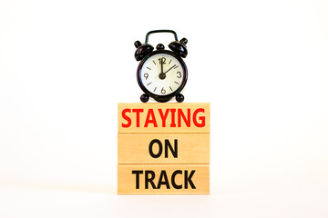 Staying on track symbol. Concept words Staying on track on wooden blocks on a beautiful white table white background. Black alarm clock. Business, motivational and staying on track concept.