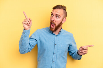 Young caucasian man isolated on yellow background pointing to different copy spaces, choosing one of them, showing with finger.