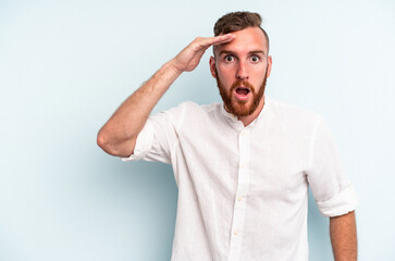 Young caucasian man isolated on blue background shouts loud, keeps eyes opened and hands tense.