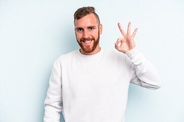 Young caucasian man isolated on blue background cheerful and confident showing ok gesture.