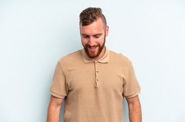Obraz premium Young caucasian man isolated on blue background laughs and closes eyes, feels relaxed and happy.