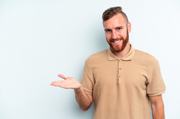 Young caucasian man isolated on blue background showing a copy space on a palm and holding another hand on waist.