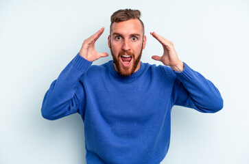 Fototapeta na wymiar Young caucasian man isolated on blue background receiving a pleasant surprise, excited and raising hands.
