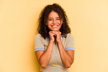Fototapeta na wymiar Young Brazilian woman isolated on yellow background keeps hands under chin, is looking happily aside.