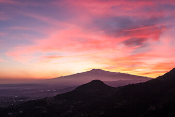 Panoramic view on silhouette of hills during twilight. Watching beautiful sunset behind volcano Mount Etna near Castelmola, Taormina, Sicily, Italy, Europe, EU. Clouds with vibrant red orange colors