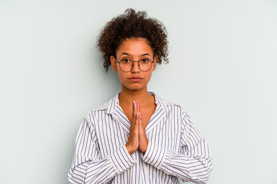 Young Brazilian woman isolated on blue background praying, showing devotion, religious person looking for divine inspiration.