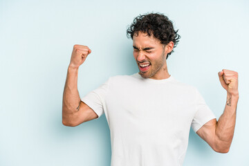 Young caucasian man isolated on blue background raising fist after a victory, winner concept.