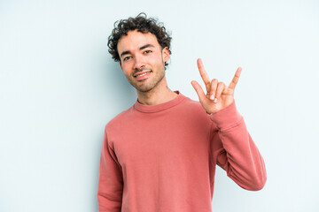 Fototapeta premium Young caucasian man isolated on blue background showing a horns gesture as a revolution concept.