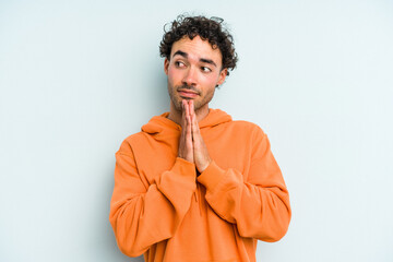 Young caucasian man isolated on blue background praying, showing devotion, religious person looking for divine inspiration.