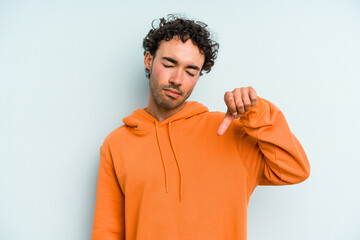 Young caucasian man isolated on blue background showing a dislike gesture, thumbs down....