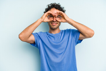 Naklejka premium Young caucasian man isolated on blue background showing okay sign over eyes