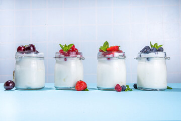 Variety of yogurts in portion glass jars. Healthy summer breakfast concept, with seasonal berry –...