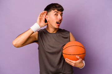 Young hispanic basketball player man isolated on purple background trying to listening a gossip.