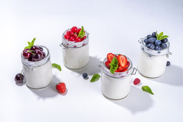 Variety of yogurts in portion glass jars. Healthy summer breakfast concept, with seasonal berry – strawberry, cherry, blueberry, currant 