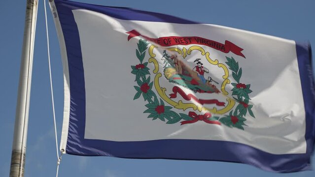 Closeup of West Virginia, WV, flag waving in slow motion in a blue sky as a symbol of the mountain state.