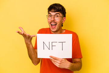 Young hispanic man holding nft placard isolated on yellow background receiving a pleasant surprise, excited and raising hands.