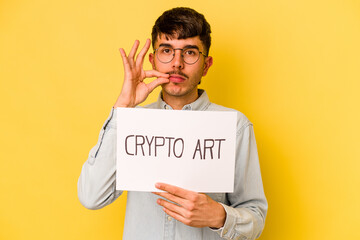 Young hispanic man holding crypto art placard isolated on yellow background with fingers on lips keeping a secret.