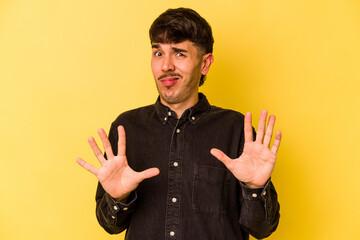 Young caucasian man isolated on yellow background rejecting someone showing a gesture of disgust.