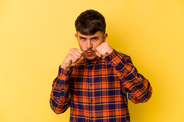 Young caucasian man isolated on yellow background throwing a punch, anger, fighting due to an argument, boxing.