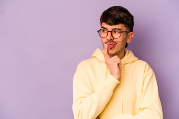 Young caucasian man isolated on purple background looking sideways with doubtful and skeptical expression.