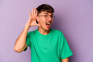 Young caucasian man isolated on purple background trying to listening a gossip.