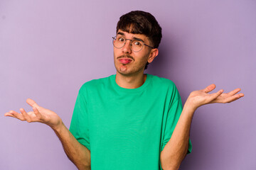 Young caucasian man isolated on purple background doubting and shrugging shoulders in questioning...