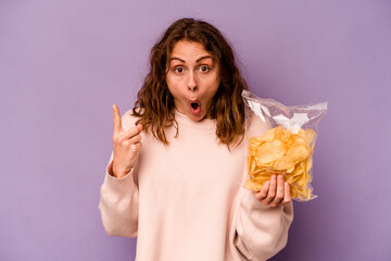 Young caucasian woman holding a bag of chips isolated on purple background having an idea, inspiration concept.