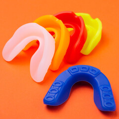 many colored boxing mouth guards lie on an orange background, concept